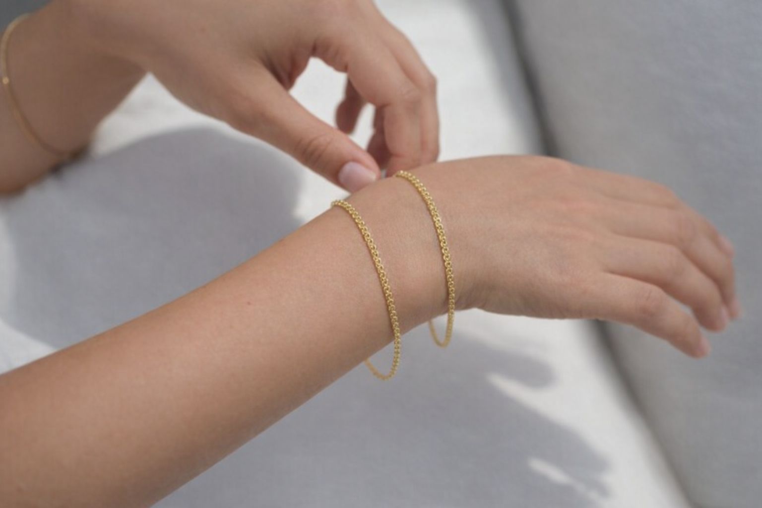 En hand med ett tunt bismarckarmband i guld runt handleden.