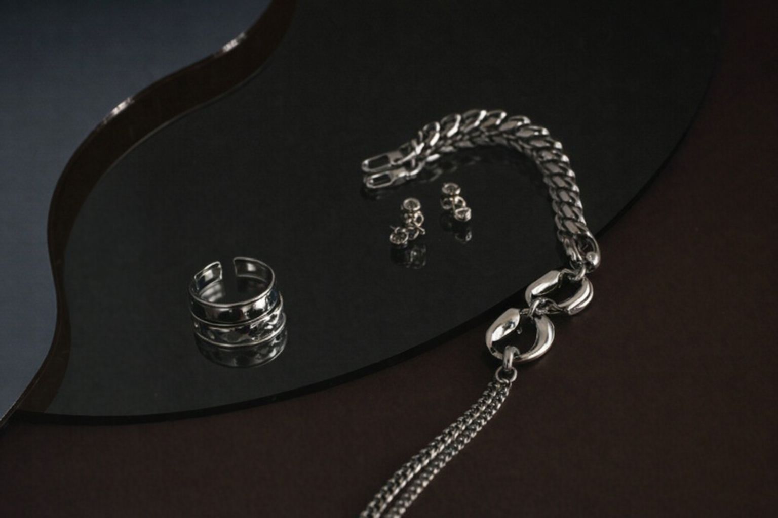 Silverfärgade smycken med en kraftig pansarlänk och ring på en mörk reflekterande yta.